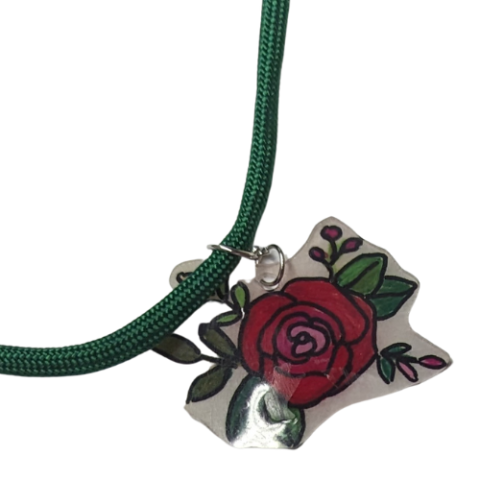 A hand outlined and colored red rose pendant made of shrinky-dink plastic on a green cord