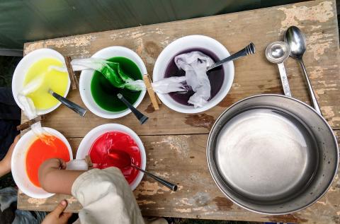 Bowls of Kool-Aid liquid in yellow, green, purple, orange and red, with silk streamers soaking in and between them.