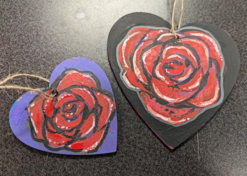 two heart-shaped ornaments, one painted purple and one black, both with roses painted on them.