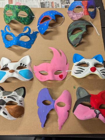 A selection of differently shaped painted paper-mache masks spread across a table. 