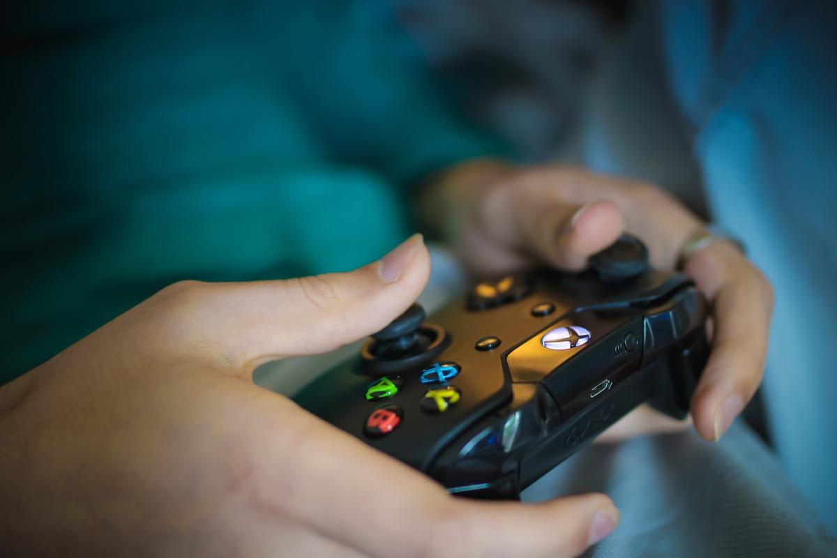 Hands holding a video game controller in front of what appears to be a blue shirt worn by the owner of the hands