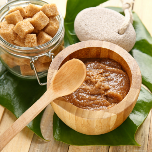 Some cubes of brown sugar, a pumice stone and a wooden bowl apparently full of sugar scrub